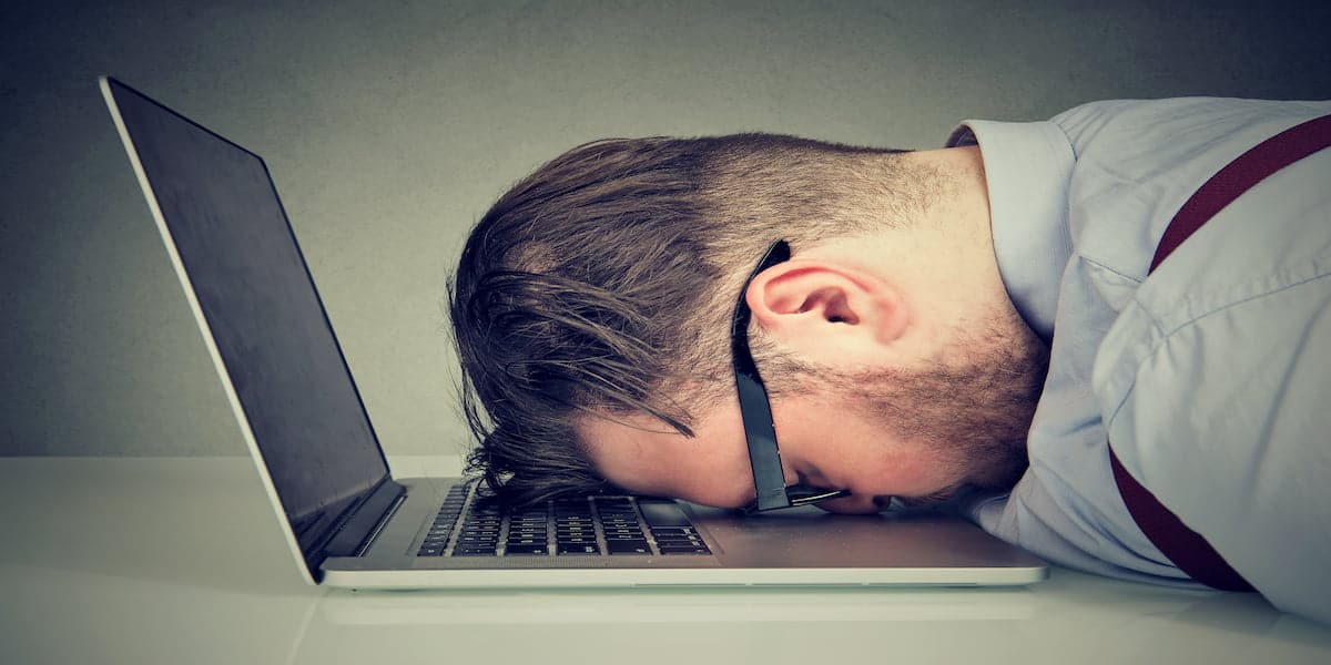 A tired businessman resting his head on a laptop keyboard, symbolizing burnout and frustration, representing the concept of "10 Reasons Why Businesses Fail and How to Avoid Them."